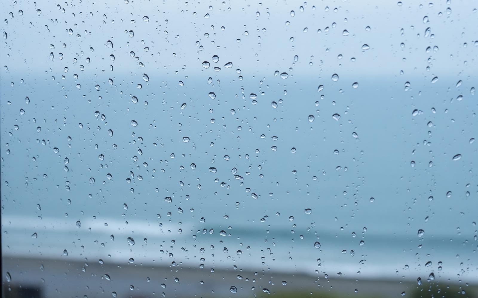 Rain on a window overlooking a blurred coastal view, reflecting the heaviness of depression